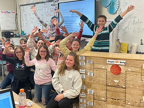 students with their hands raised in the air standing and sitting near tournament bracket board