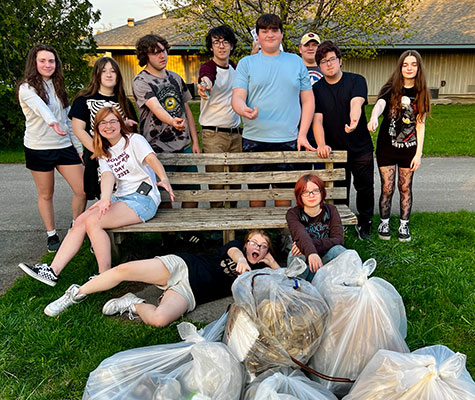 group of students sitting behind several full trash bags