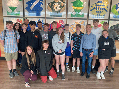 students standing in a group in front with jockey of display of racing silks