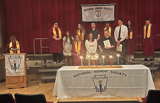 student speaking at podium while NHS member students stand in a group on stage