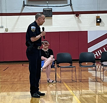 police officer talking into microphone to students in gym