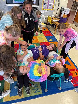 students setting up a group activity involving chairs and supporting each other