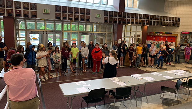 big group of 6th grade students in HS lobby, listening to Ms. Mahoney