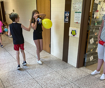 student blowing up balloon on car in hallway