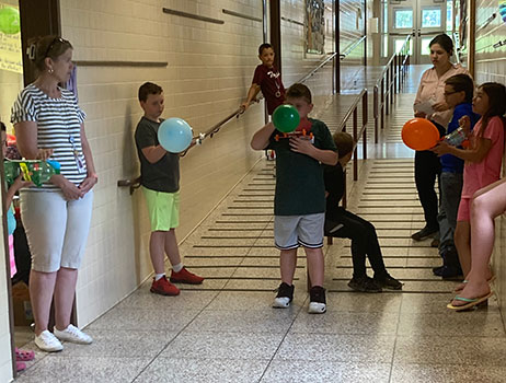 student blowing up balloon on car in hallway