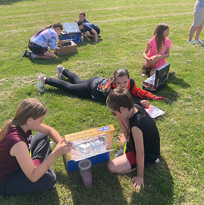 students on lawn using solar ovens