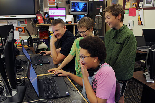 students and teacher looking at computer screen and smiling