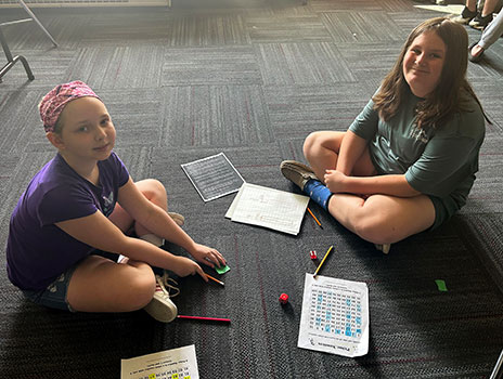 students seated on floor engaging in a math game on paper