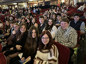 Dozens of Fort Plain High School students sit in plush, dark red seats at Proctor's Theatre in Schenectady before a producation of Mrs. Doubtfire. All are looking at and smiling for the camera.