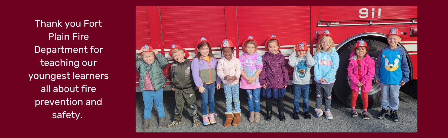A photograph of a group of kindergarten students wearing firefighter hats and stand in a line in front of a bright red firetruck is featured at the right of this image. The phrase: Thank you Fort Plain Fire Department for teaching our youngest learners all about fire prevention and safety is featured at left. The background of this image is dark red.